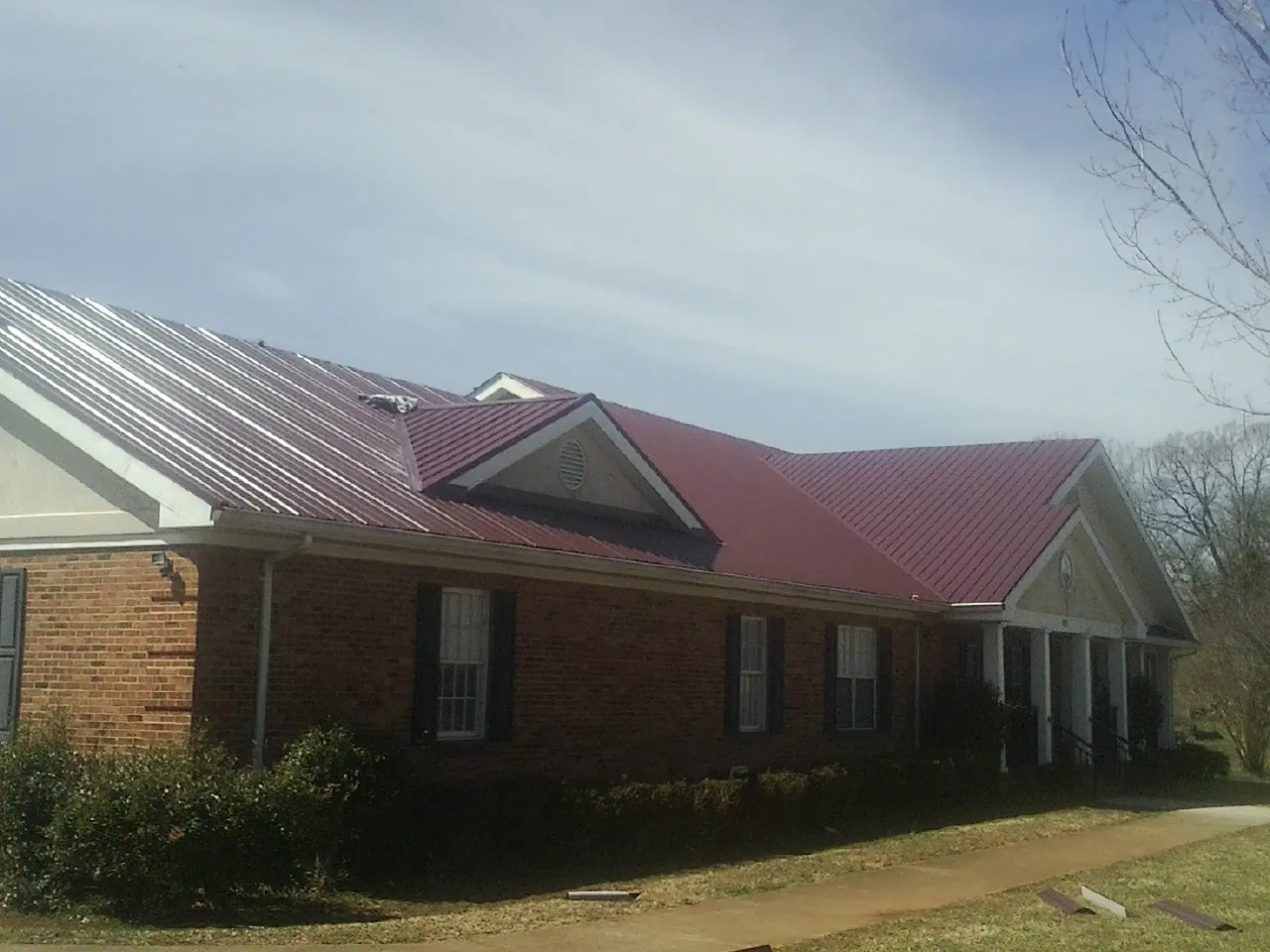 Red metal roof with gabled entries on a long brick building, from a Hail Damage Roof Repair job in Steger