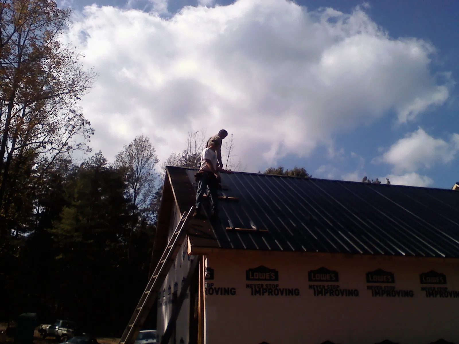 Roofer fastening dark metal panels high against a cloudy sky, from a Roof Inspection job in Steger